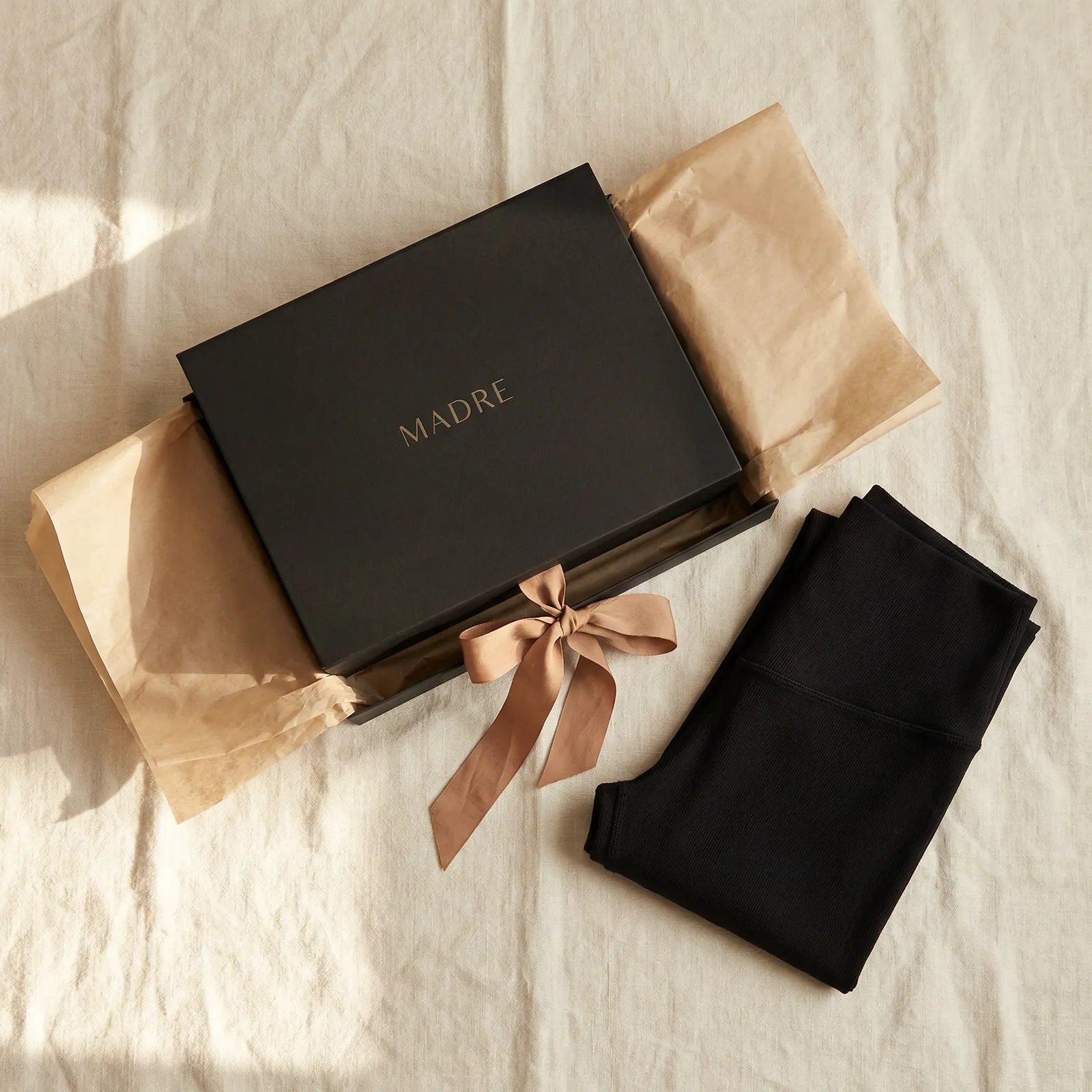 MADRE black gift box with a satin ribbon, tissue paper and folded black recovery wear on linen